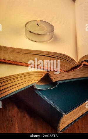 Lesung in der Dunkelheit bei Kerzenschein. Ein Stapel alter Bücher mit einer brennenden Kerze und ein Platz für Text, selektiver Fokus, getönten Bild Stockfoto