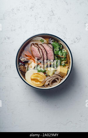Miso Ramen mit gebratenem Rindfleisch, Shiitake-Pilze, gebratenem Tofu, Lauch und Eier auf konkreten Hintergrund. Ansicht von oben. Im asiatischen Stil Mittagessen Stockfoto