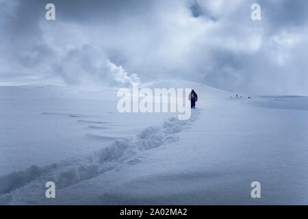 Mann, der durch den tiefen Schnee zu den Dampffumarolen auf dem Berg Asahi, Hokkaido, Japan, geht Stockfoto