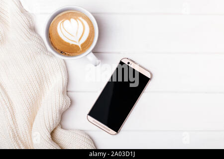 Kaffee, Telefon mit leeren schwarzen Display und gestrickte Pullover auf dem weißen Tabelle, Ansicht von oben Stockfoto