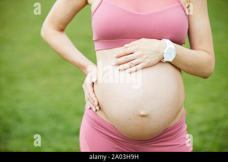 Close-up von jungen schwangeren Frau in rosa Top stehen im Freien und genießen das gute Wetter Stockfoto