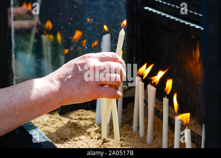 Der Frau die Hand die brennende Kerze mit Reflexion auf das Glas in der Kirche. Religion. Stockfoto