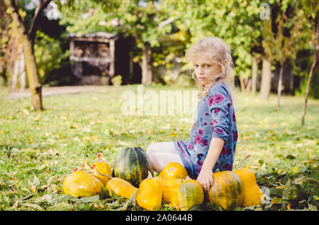 Schönes Kind sitzen über orange Kürbis draußen im grünen Garten Stockfoto