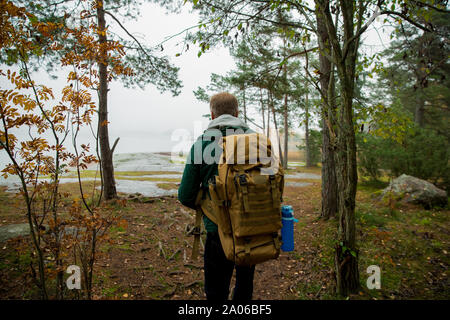 Reifer mann Finnland erkunden im Herbst, in Nebel. Wanderer mit grossen Rucksack auf bemoosten Felsen. Skandinavische Landschaft mit misty Meer und Stockfoto