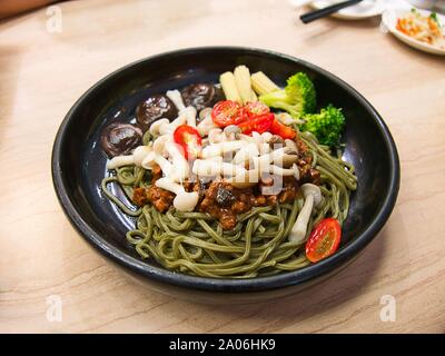 Vegetarische Matcha/grüner Tee Nudeln mit Gemüse und herzhaften tofu Sauce in schwarz Schüssel auf hölzernen Tisch Stockfoto