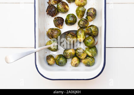 Brassica oleracea. Gerösteter Rosenkohl in weißer Emaille braten Teller mit Löffel auf einem weißen Holz- Hintergrund Stockfoto