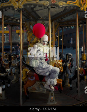 Ein Mann in das Bild eines Clowns reitet ein Karussell auf ein Pferd mit einem roten Ballon in der Hand. Stockfoto