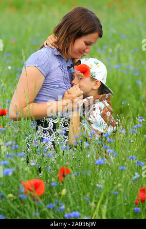 Sommer Portrait von gerne kuscheln Mutter und Sohn im blühenden Mohn Feld Stockfoto