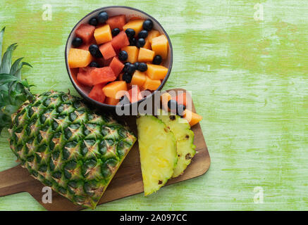In Scheiben geschnittene Ananas und Obstschale auf grünem Holz- Hintergrund. Ansicht von oben. Stockfoto