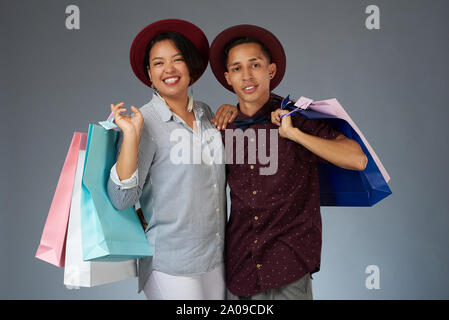 Junge hispanic Paar mit Einkaufstaschen auf grauem Hintergrund Stockfoto