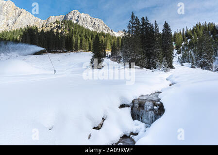 Winterlandschaft in den österreichischen Alpen. Gefrorene Creek umgeben von Schneeverwehungen und verschneiten Tannen. Stockfoto