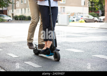 Untere Partie des jungen Paares Reiten auf der Elektroroller Auf der Stadt. Stockfoto