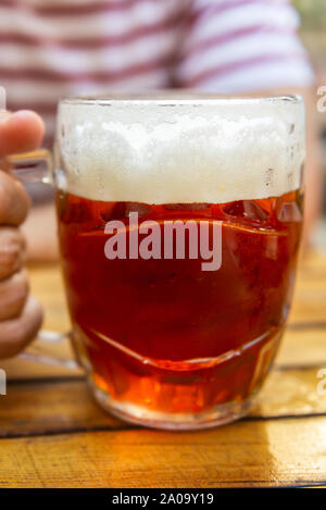 Der Mensch ist ein frisch gezapftes Glas Bier in der Hand Stockfoto