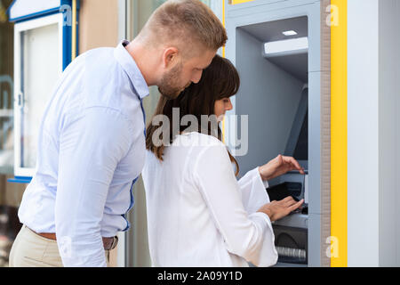 Man Spionage für PIN-Code, während Frau mit Geldautomaten für Geld abheben Stockfoto