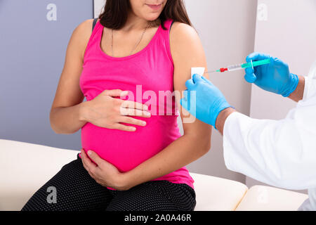 Nahaufnahme der Arzt trägt blaue Handschuhe Impfung von jungen schwangeren Frau in Klinik Stockfoto