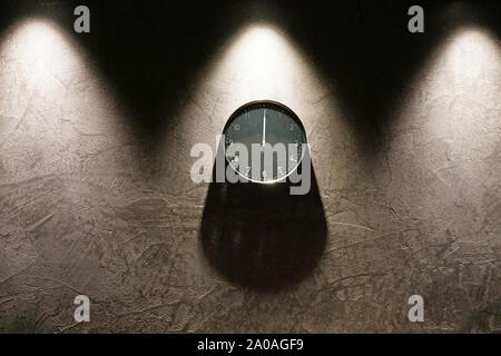 Schwarz Einfache analoge Uhr zeigt 24:00 Uhr hängen an der dunkelbraunen Mauer mit Kopie Raum um. Zwei Dreieck Schatten von oben und eine abgerundete Shad Stockfoto