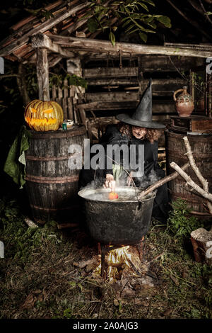 Alte Hexe brauen tödlichen Trank für Halloween in einen gusseisernen Topf Stockfoto