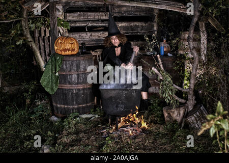Alte Hexe brauen tödlichen Trank für Halloween in einen gusseisernen Topf Stockfoto
