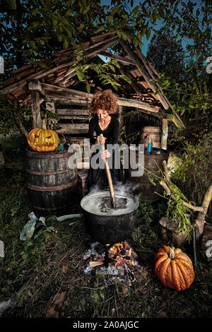 Alte Hexe brauen tödlichen Trank für Halloween in einen gusseisernen Topf Stockfoto