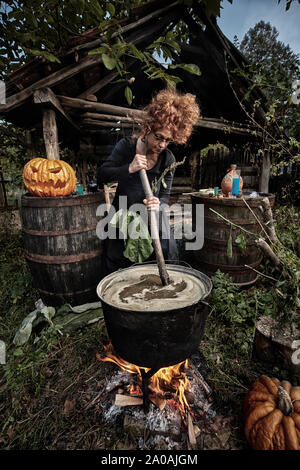 Alte Hexe brauen tödlichen Trank für Halloween in einen gusseisernen Topf Stockfoto