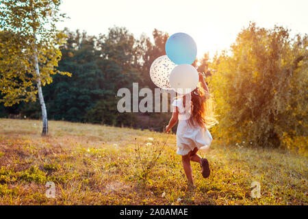 Mädchen mit Luftballons in der Hand. Glückliches Kind Spaß im Sommer Park bei Sonnenuntergang. Aktivitäten im Freien Stockfoto