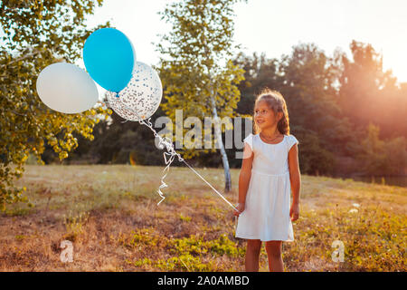 Gerne kleine Mädchen mit Luftballons in der Hand. Kind Spaß im Sommer Park bei Sonnenuntergang. Stockfoto