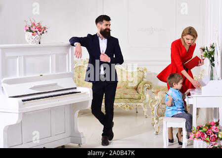 Heimschule Konzept. Kid growthing in der Wohlfahrt. Die Eltern genießen die Elternschaft, sorglos, glücklich. Vater steht in der Nähe von Piano, aufpaßt, während Mutter teache Stockfoto