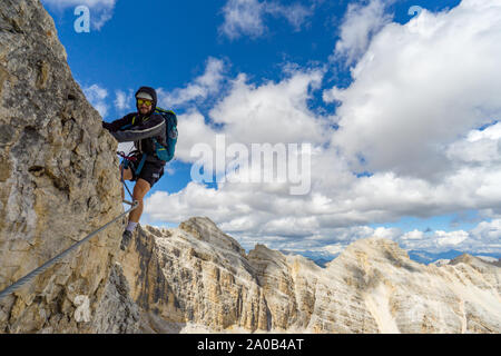 Jungen gutaussehenden männlichen Bergsteiger auf einem steilen und exponierten Fels klettert ein Klettersteig in Alta Badia in Südtirol Stockfoto