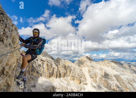 Jungen gutaussehenden männlichen Bergsteiger auf einem steilen und exponierten Fels klettert ein Klettersteig in Alta Badia in Südtirol Stockfoto