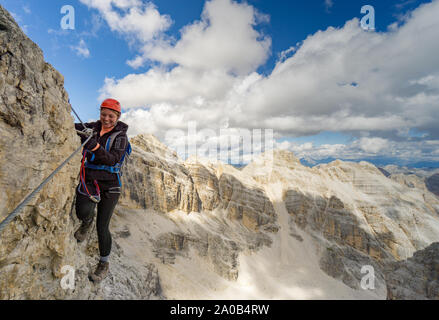 Horizontale Ansicht einer attraktiven Blondine weiblichen Kletterer auf einem steilen Klettersteig in den italienischen Dolomiten mit tollem Blick hinter Stockfoto