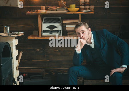 Intelligenter Kerl in der Studie Zimmer sitzen. Bärtige blonder Mann im blauen Anzug lehnte sich auf seine Hand beim Denken an eine Vorstellung. Stockfoto