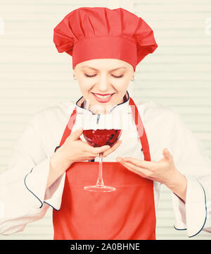 Somellier mit Weinglas. Frau in Cook hat und Schürze. professioneller Koch in der Küche. Küche. Hausfrau Rotwein trinken. glückliche Frau. Grüße an Freunde. Sommelier Prüfung Wein. Das ist perfekter Wein. Stockfoto