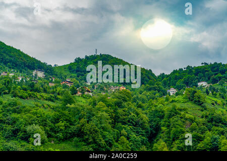 Häuser zwischen Bäumen auf einem Hügel im Schwarzen Meer Region während einem bewölkten Tag und die Sonne sich hinter Wolken gesehen werden. Stockfoto