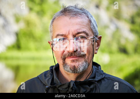 Close up Portrait eines älteren intelligenter Mann in Gläsern und mit einem grauen Bart. Lächelnde Gesicht eines gebildeten Menschen im Rentenalter. Outdoor Portrait Stockfoto