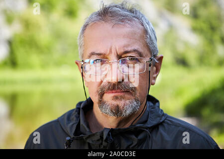 Eine Nahaufnahme Porträt eines intelligenten älterer Mann mit einem ernsten Gesicht, Gläser mit einer dünnen Metallrahmen, einen grauen Bart und einem kurzen Haarschnitt. Foto von einem Stockfoto