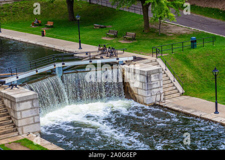 Wasser läuft über den Rand eines Schlosses in einen Kanal. Steinerne Treppen und Mauern der Schlösser, die von einer öffentlichen Parkanlage umgeben sind. Stockfoto