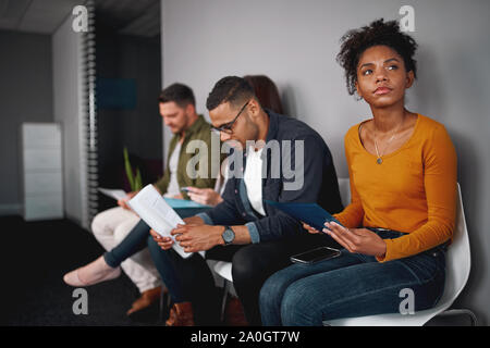 Arbeitslose junge afrikanische amerikanische Frau Stress über mühsame Warten in Warteschlange mit anderen Kandidaten für Vorstellungsgespräch sitzen Stockfoto