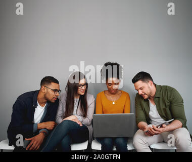 Gruppe von diversen Freunden sitzen auf Stühlen in der Warteschlange Videos online oder über Social Media App auf Laptop Stockfoto