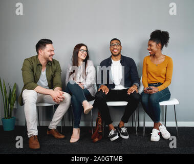 Vielfältige Gruppe von Freunde sitzen auf Stuhl, die in der Warteschlange warten, lächelnd und gemeinsam genießen - junge Gruppe von Freunden erleben Sie ein Gefühl der Zugehörigkeit Stockfoto