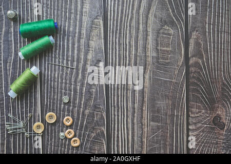 Nähzubehör auf dunklem Hintergrund. Grüne Nähgarne, Nadel, Buttons und Pins. top Aussicht, flatlay Stockfoto