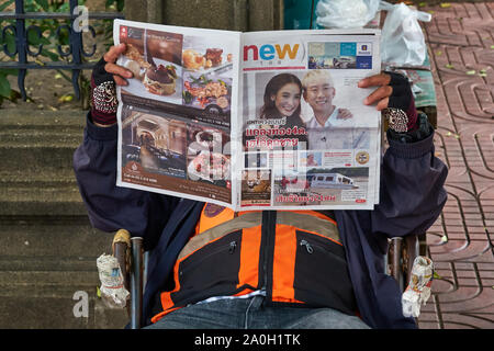 Ein Motorrad Taxi driver in Bangkok, Thailand, absorbiert Lesen einer lokalen Zeitung Stockfoto