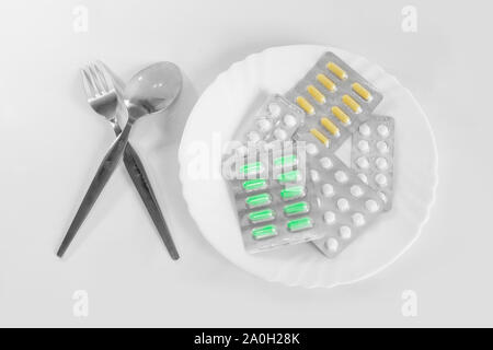 Verschiedene Tabletten auf einem Teller mit Besteck. Das Konzept der verschreibungspflichtigen Medikamente zur Gewichtsreduktion. Mittel zur Unterdrückung des Appetits. Stockfoto