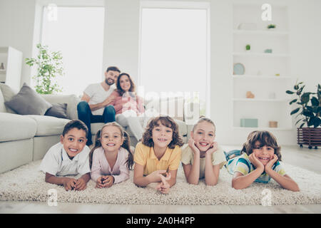 Nahaufnahme von multinationalen Zwillinge Kinder Blick auf Kamera Mama mama Mama Und große toothy Lächeln machen, lag auf weichen Teppich boden in der Nähe unscharf gemütliche Couch mit Ha Stockfoto