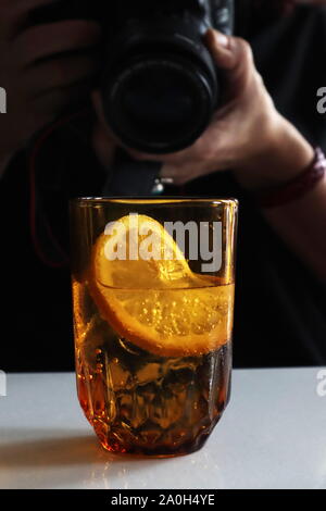 Fotografin mit Canon DSLR-Kamera fotografieren golden Glas Wasser mit Kohlensäure mit zitronenscheibe Stockfoto