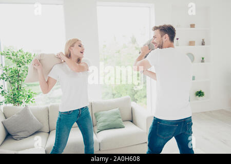 Schöne attraktive adorable Bezaubernd, charmantes, niedlich netten Paar in der beiläufigen weiße T-Shirts und Jeans, kämpfen mit Kissen, helle Einrichtung Stockfoto