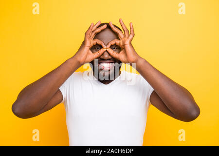 Schöne attraktive Manly heiter froh dumm mulatto Mann mit strahlenden Lächeln wie Gläser Geste, die über helle leuchtend gelben backgr isoliert Stockfoto