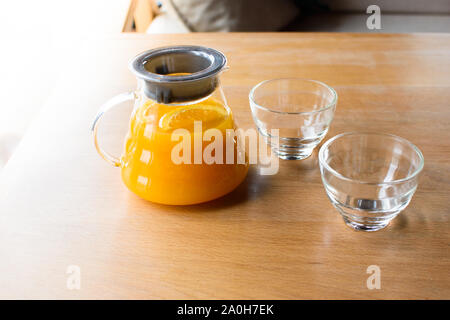 Teekanne von orange Früchte Tee und zwei Glas Tassen in einem hölzernen Tisch in einem Cafe. Stockfoto