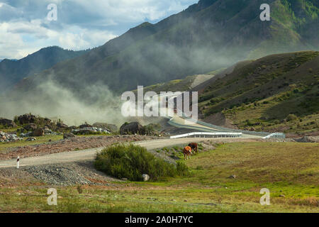 Landschaft in den Bergen des Altai, durch zwei große Lastwagen mit Schutt aufgefüllt gestört, für die Hill, eine große Menge von schmutzigen Staub fliegt und Stockfoto