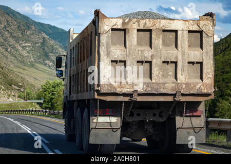 Ansicht von hinten auf einem großen Dump Truck fährt auf einer Autobahn in den Bergen beim Transport von Gütern über große Entfernungen. Schnelle Lieferung durch Masse transportati Stockfoto