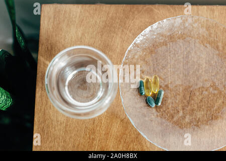 Omega 3, Spirulina, Chlorophyll Kapseln und Glas Wasser auf Holztisch. Nahrungsergänzungsmittel, biologisch aktive Zusätze. Morgen vitamin Pillen Stockfoto